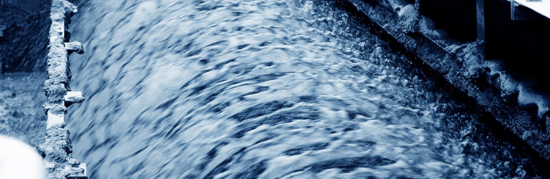 Close-up image of turbulent wastewater flow through an industrial treatment channel, representing the regulatory and treatment challenges addressed during ARCO/Murray and BlueWTR’s consulting engagement for Project BenchPress.