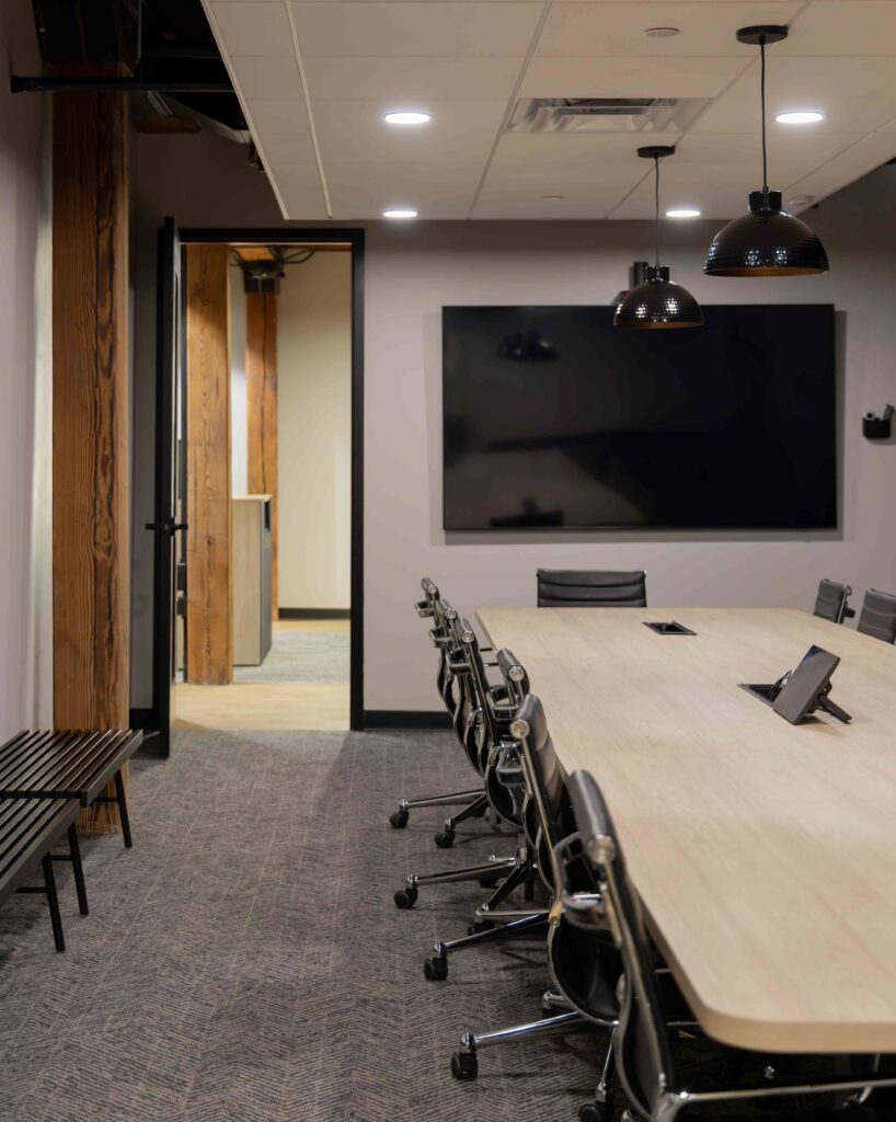 Conference room in Branigan’s Milwaukee office with a long wood table, leather task chairs, and a large wall-mounted screen for presentations.