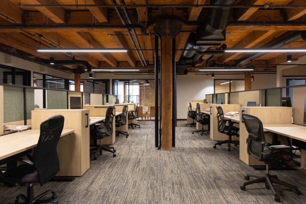 Open office area in Branigan’s new Milwaukee headquarters with rows of light wood workstations, ergonomic chairs, and exposed timber beams overhead