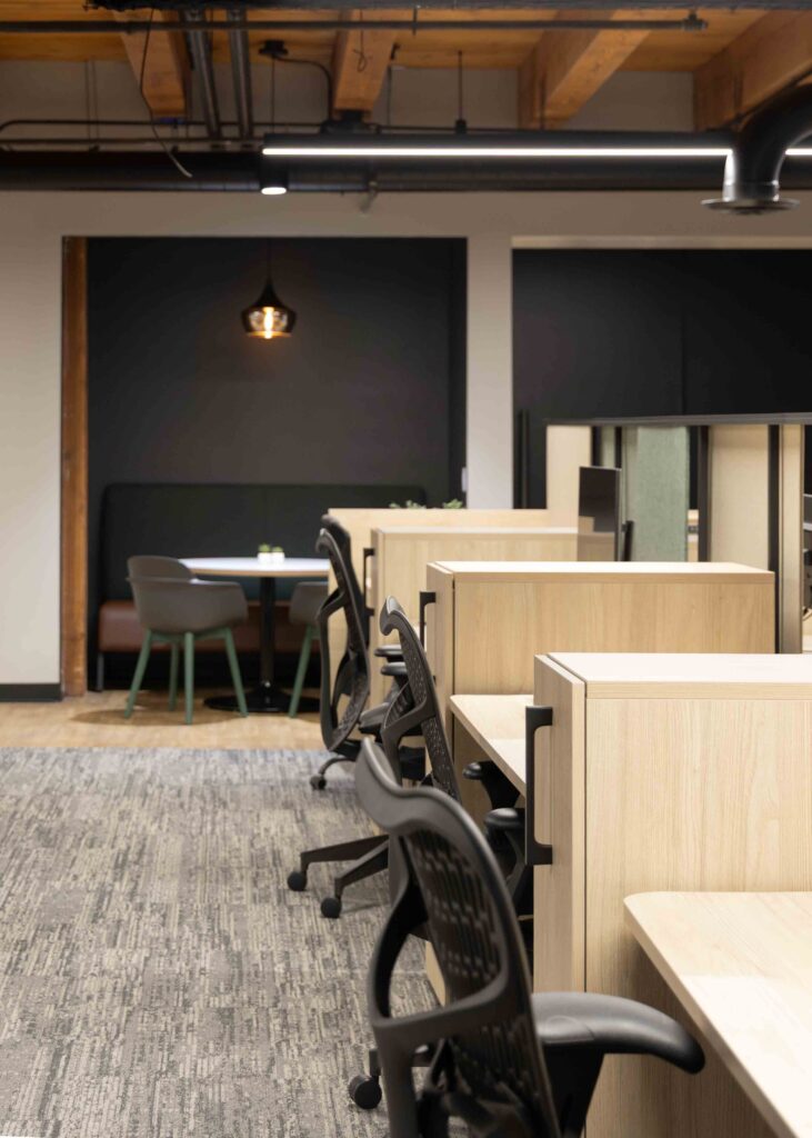 Row of open workstations in Branigan’s Milwaukee office with a booth-style seating nook and pendant light in the background.