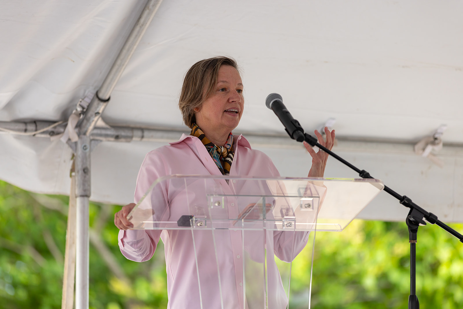 Delphine Lenoir speaks at a clear podium under a tent during the Orion STEM Schools groundbreaking event.