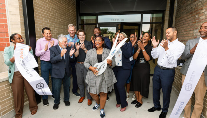 Group celebrating outside a Chicago Collegiate Charter School entrance, with a woman holding oversized scissors as others applaud beside a ceremonial ribbon.